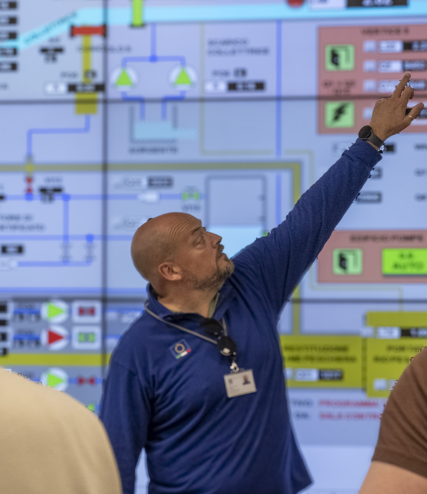 Uomo indica uno schermo con diagrammi e controlli industriali