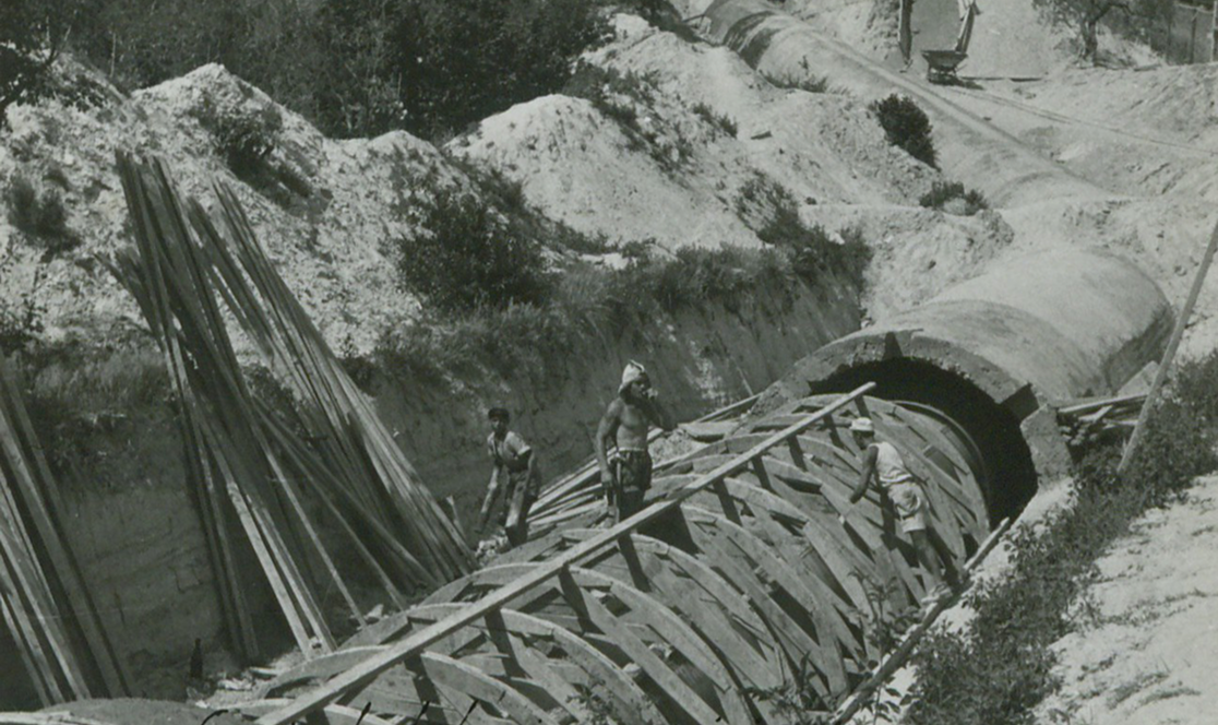 Operai al lavoro sulla posa delle casseforme in legno per la realizzazione di una condotta in cemento. In primo piano, le centine curve della struttura; sullo sfondo, l'imbocco di una galleria scavata nel terreno. Anno 1945.